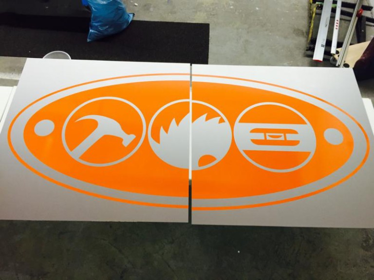 Folienbeschriftetes Schild mit orangem Logo der Tischlerei Bauer