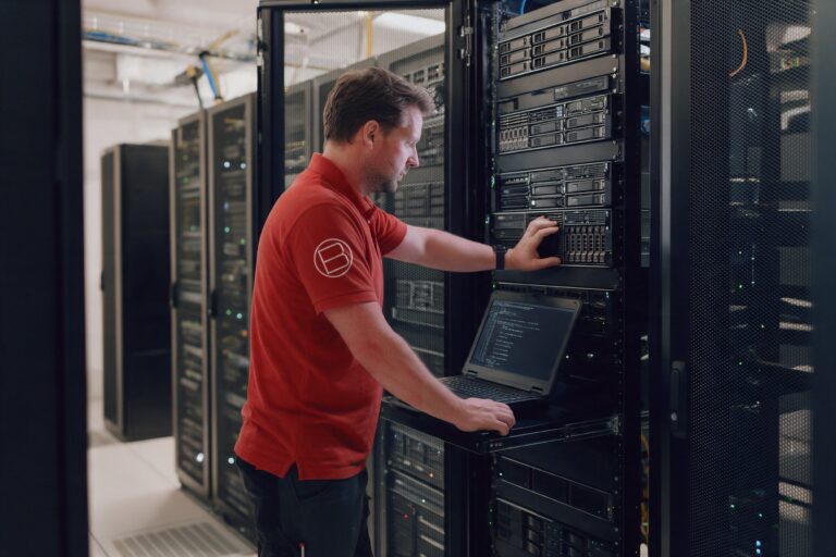 Techniker im roten Poloshirt prüft einen Server am offenen Serverschrank